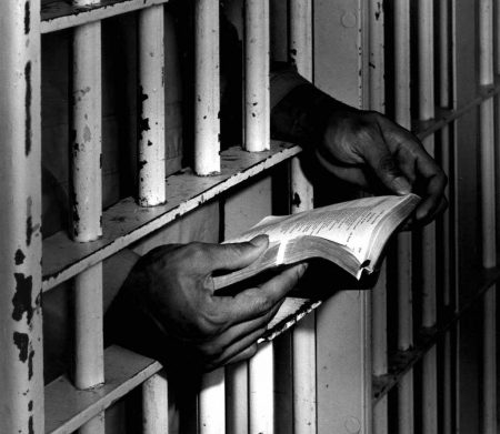 Hands held out through prison bars, holding a book